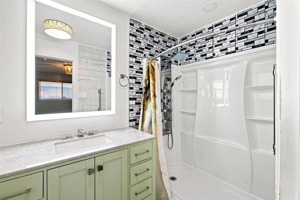 2022 Normandy Drive, Irving, TX 75060 Illuminated vanity mirror, light green custom cabinetry, white countertop with integrated sink, black and white mosaic tile shower surround, and white shower enclosure