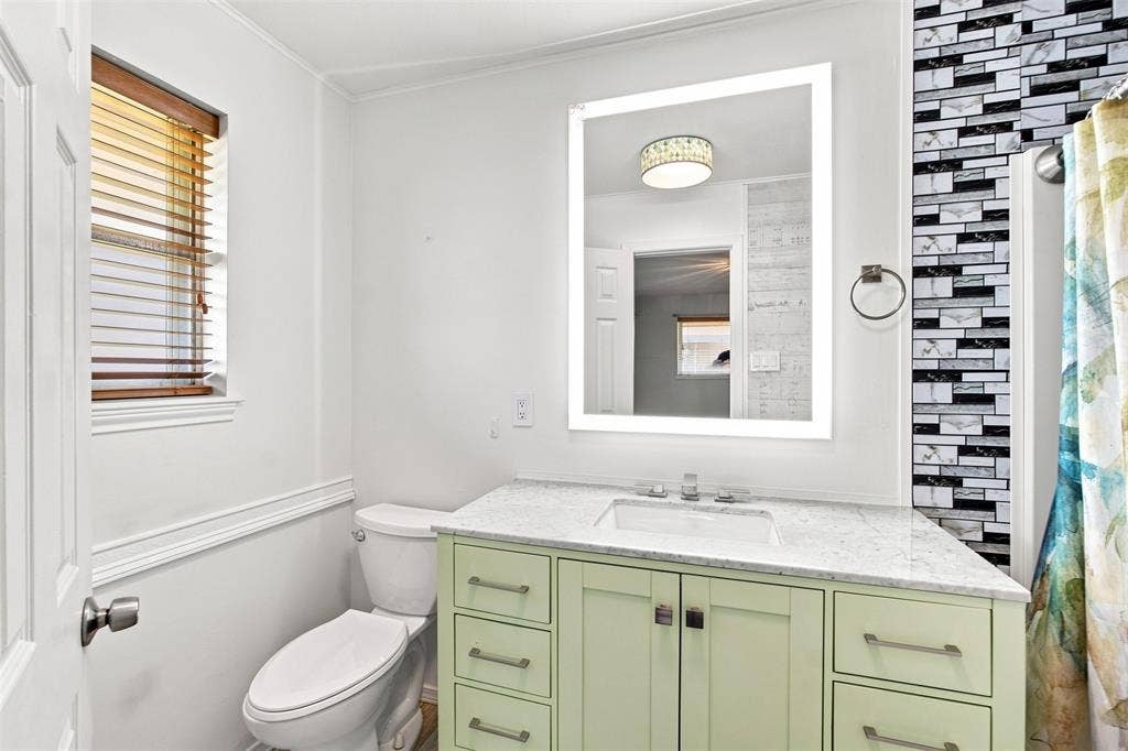 2022 Normandy Drive, Irving, TX 75060 Bathroom vanity with a white countertop and integrated sink, illuminated mirror, and a decorative tiled wall