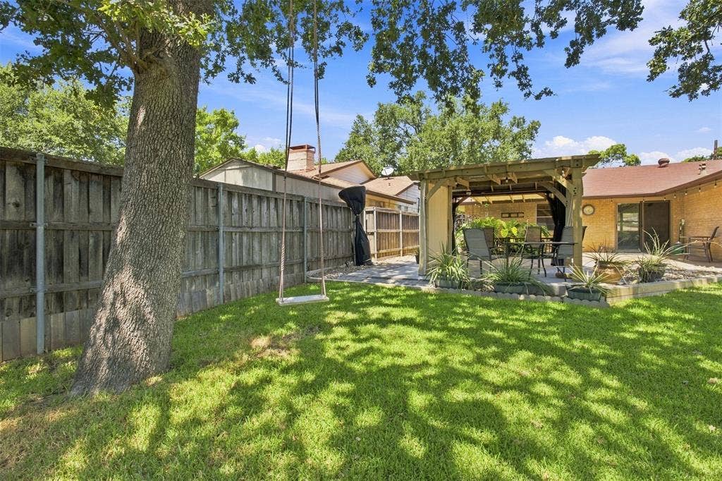 2022 Normandy Drive, Irving, TX 75060 Expansive backyard featuring a manicured lawn, a built-in wooden pergola, swing, and a privacy fence