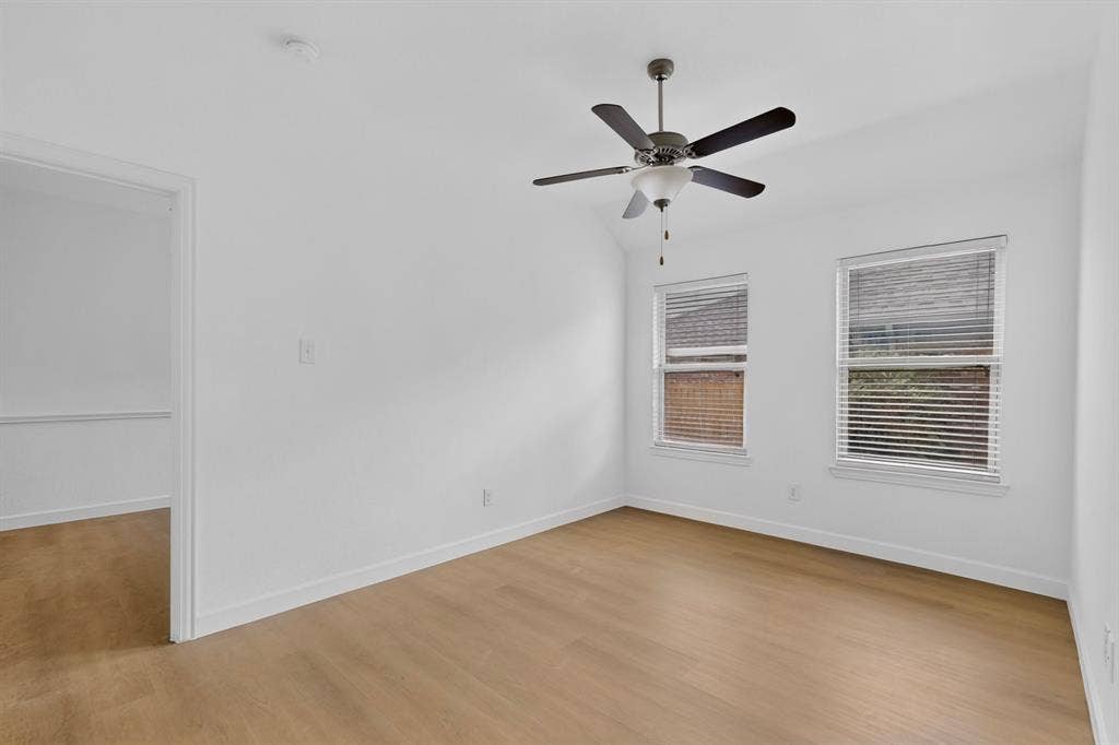 Interior room featuring wood-finish flooring, two dual-pane windows with horizontal blinds, a vaulted ceiling, and a ceiling-mounted fan with integrated lighting