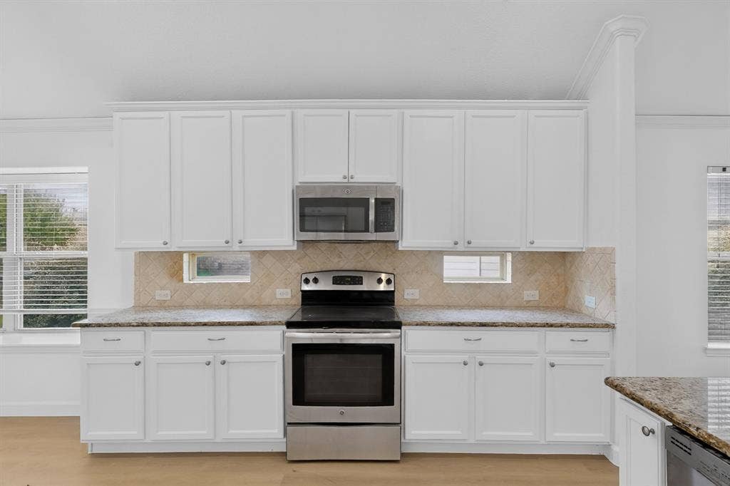 Kitchen featuring white cabinetry, stone-finish countertops, herringbone-pattern tile backsplash, stainless steel appliances, and integrated small windows