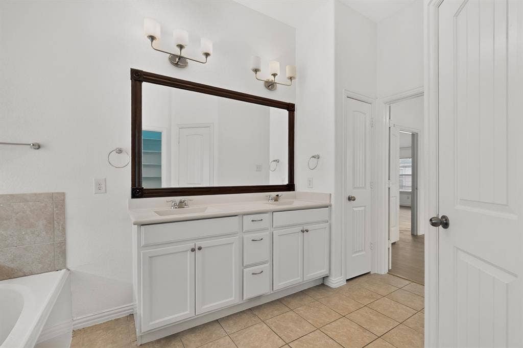 Double-sink vanity featuring a neutral countertop, white cabinetry with integrated storage drawers, a large dark-framed mirror, and dual wall-mounted light fixtures with glass shades