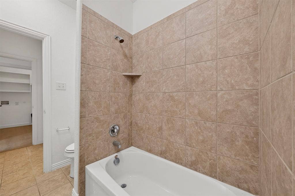 Bathtub featuring a white acrylic finish, integrated shelving, metallic fixtures, and full-height wall tile surrounds