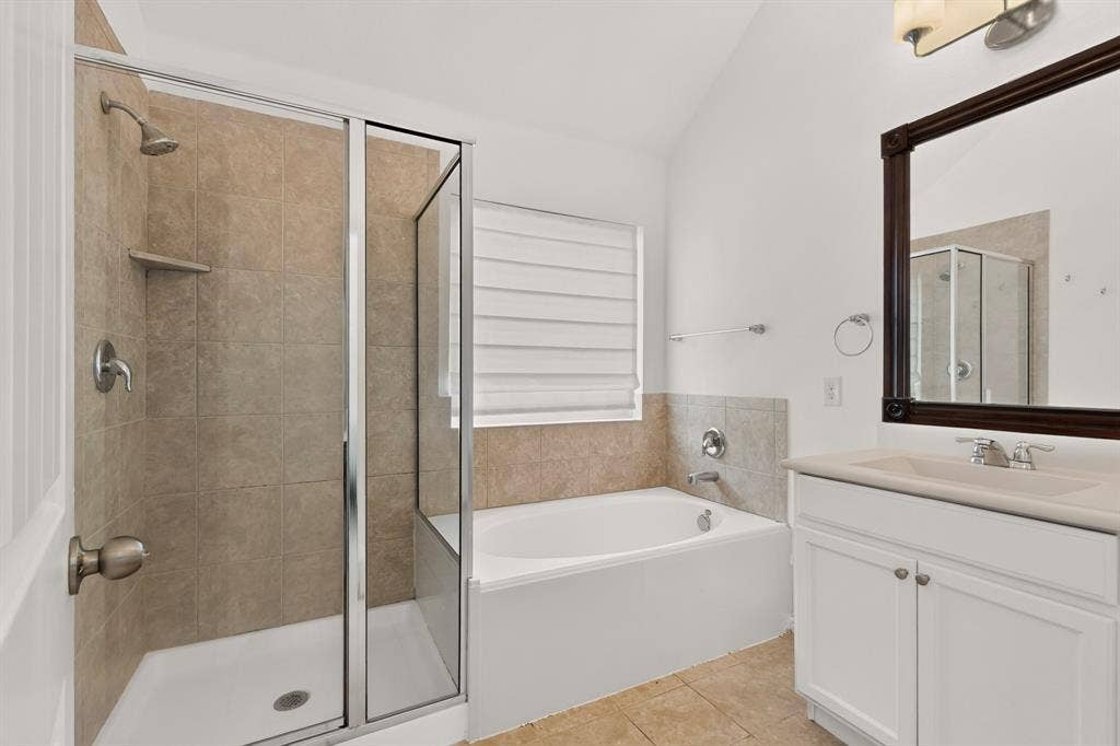 Bathroom featuring a glass-enclosed shower, built-in soaking tub with tile surround, white vanity cabinet, and vaulted ceiling