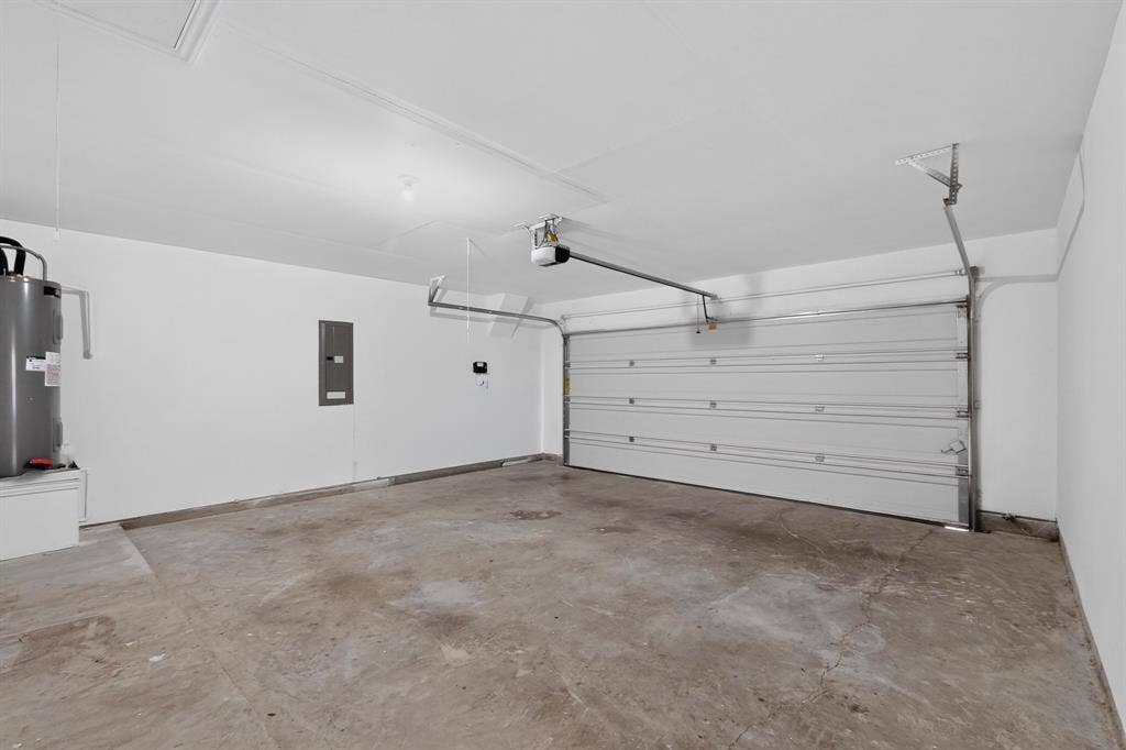 Enclosed garage featuring concrete flooring, white walls, overhead door opener, and integrated electrical panel