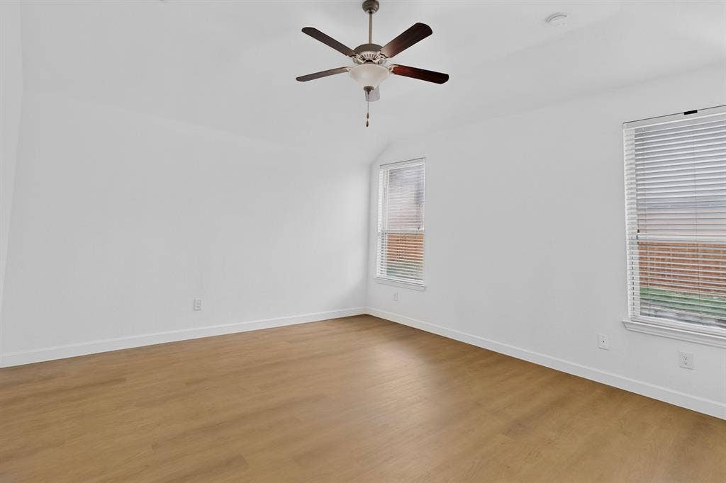Neutral wall color palette, wood-finish flooring, dual windows with horizontal blinds, and a central ceiling fan