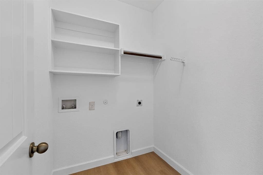 Utility area featuring wood-finish flooring, white built-in shelving, a wall-mounted garment rod, and plumbing hookups