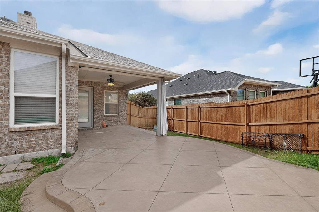 Covered patio featuring a scored concrete floor, recessed ceiling fan, brick exterior finish, and surrounding wood privacy fencing