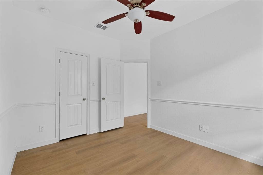 Interior space featuring wood-finish flooring, chair rail molding, two-panel interior doors, and a ceiling fan with integrated lighting