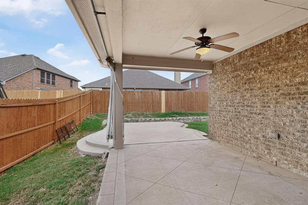 Covered patio featuring scored concrete flooring, a ceiling fan, a brick exterior wall, and a wood privacy fence