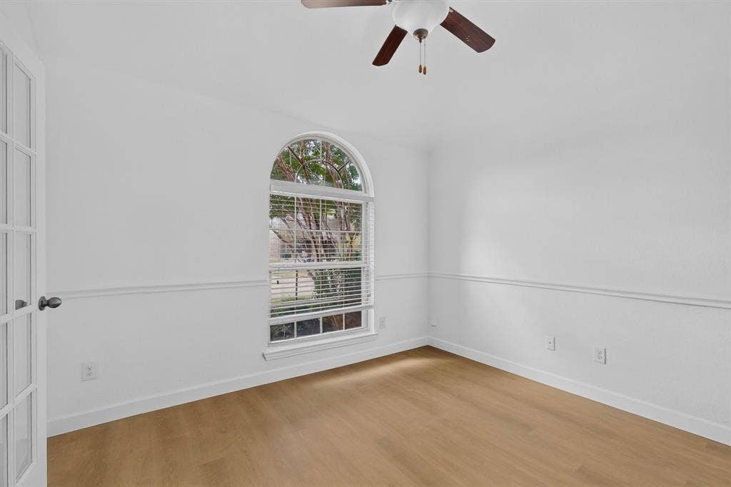 Room featuring wood-finish flooring, an arched window, chair rail molding, a multi-pane glass door, and a ceiling fan