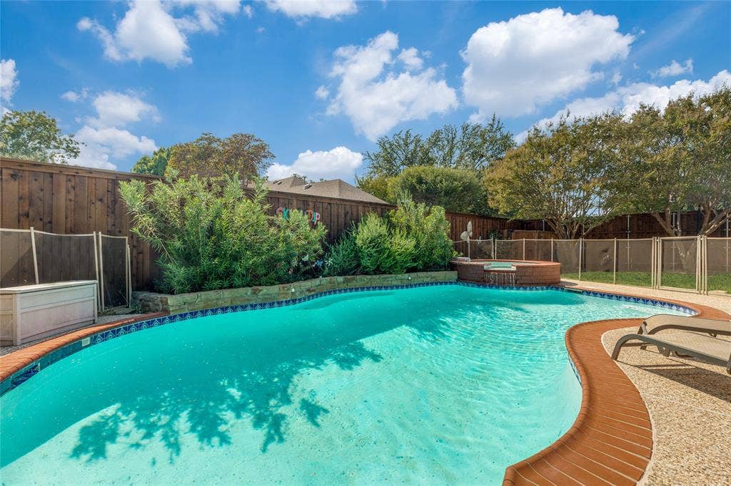 5013 Country Place Drive, Plano, TX 75023 Sparkling swimming pool with a curved design, adjacent hot tub with waterfall feature, stone-edged planting beds, and a wood privacy fence