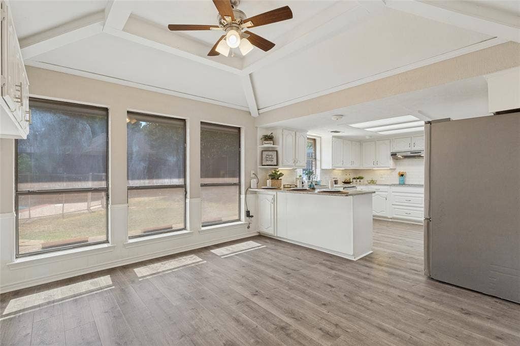 5013 Country Place Drive, Plano, TX 75023 Open-concept kitchen and dining area featuring vaulted ceilings with exposed beams, wood-finish flooring, a ceiling fan, and white cabinetry