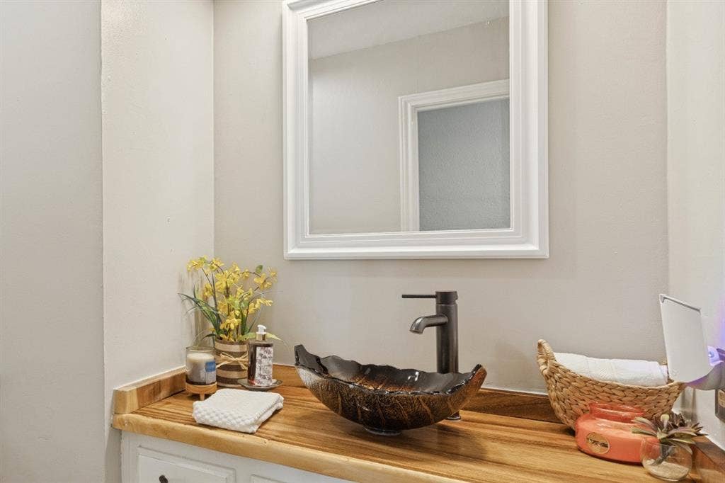 5013 Country Place Drive, Plano, TX 75023 Wood-finish countertop with a vessel sink, dark bronze faucet, and a framed wall mirror