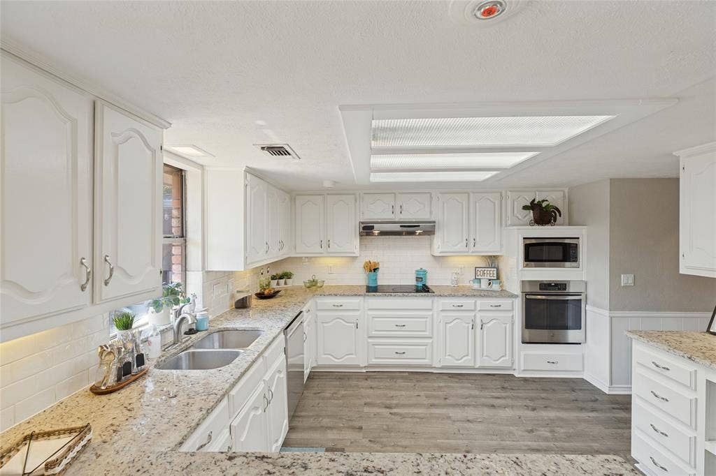 5013 Country Place Drive, Plano, TX 75023 Kitchen featuring white cabinetry, light-toned countertops, a double basin sink, stainless steel built-in appliances, and wood-finish flooring, granite countertops