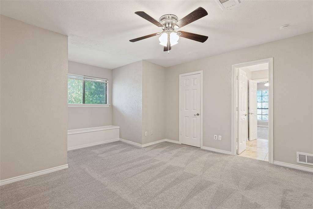 5013 Country Place Drive, Plano, TX 75023 Spacious upstairs bedroom with light neutral wall tones, gray carpeting, a built-in window bench, and a ceiling fan with integrated lighting, attached Jack & Jill Bath