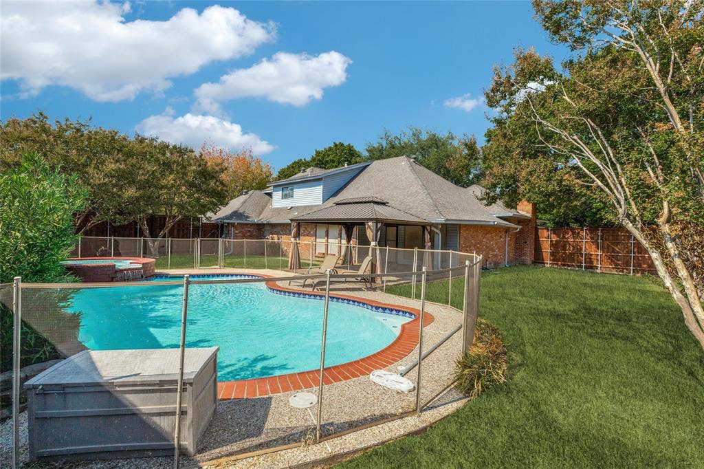5013 Country Place Drive, Plano, TX 75023 Backyard featuring a freeform swimming pool, integrated spa, surrounding stone aggregate decking, and a privacy fence