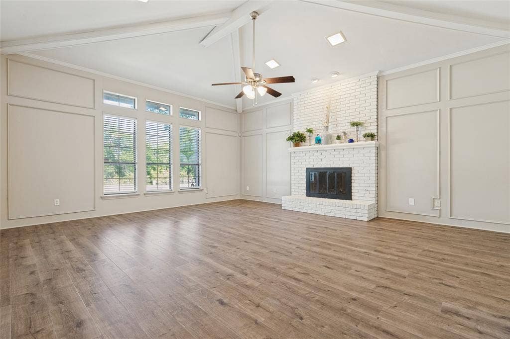 5013 Country Place Drive, Plano, TX 75023 Vaulted ceiling, wood-finish flooring, white brick fireplace with gas starter, picture frame wall paneling, and a ceiling fan with integrated lighting, large windows with park view