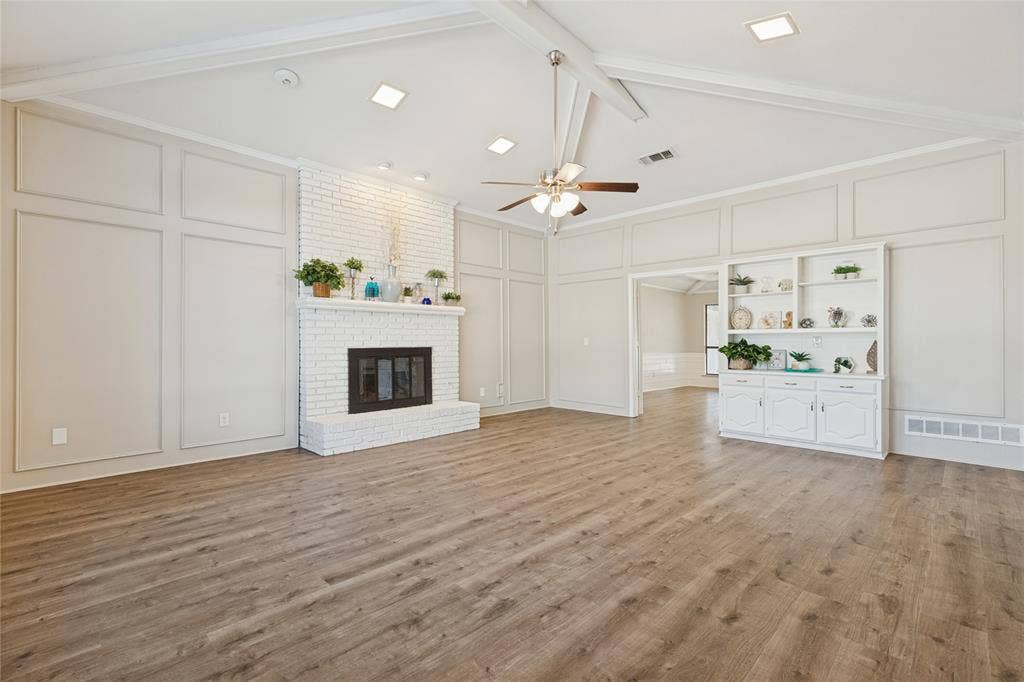 5013 Country Place Drive, Plano, TX 75023 Vaulted ceiling with exposed beams, wood-finish flooring, white brick fireplace, decorative wall paneling, and built in hutch with cabinets