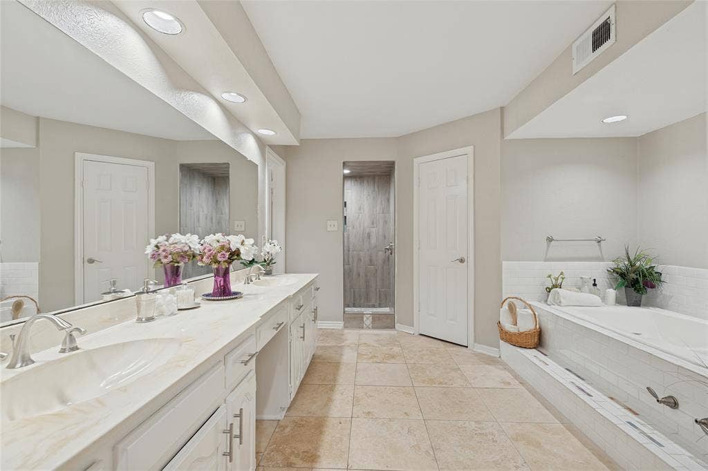 5013 Country Place Drive, Plano, TX 75023 Dual vanity with integrated sinks and extensive countertop space, cabinet storage, vanity area, two separate walk in closets, recessed lighting, built-in bathtub with subway tile surround, and a walk-in shower with custom porcelain tile design, travertine tile flooring