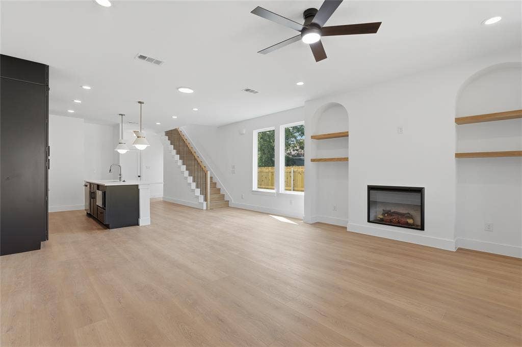 3300 S Harwood Street, Dallas, TX 75215 Open-concept living space with light wood-finish flooring, recessed lighting, and a modern fireplace with built-in arched shelving