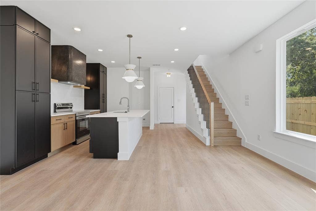 3300 S Harwood Street, Dallas, TX 75215 Open-concept kitchen with a white island, light wood-finish flooring, and a modern staircase featuring black spindles and a wood handrail