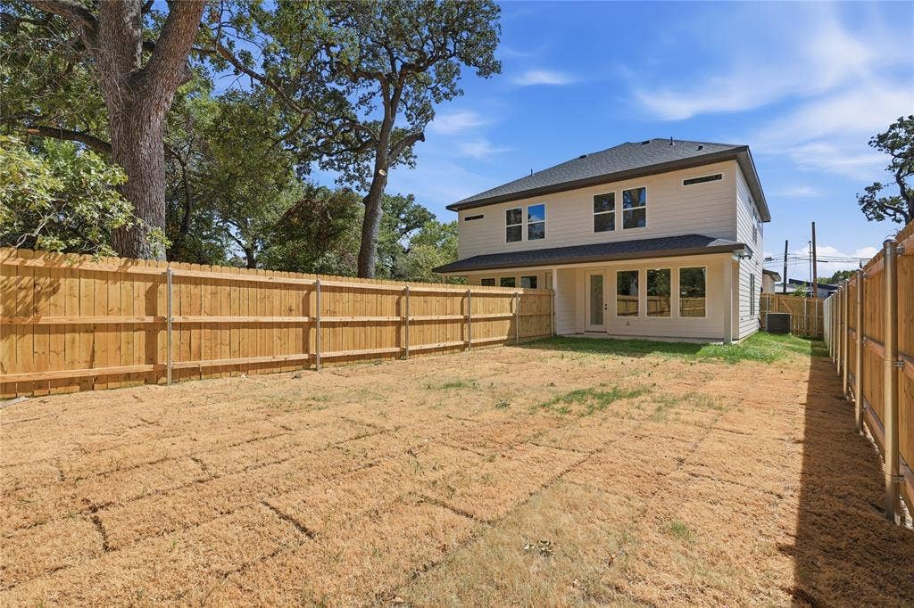 3300 S Harwood Street, Dallas, TX 75215 Expansive backyard with a full privacy fence, established trees, and a two-story residence featuring multiple windows and a rear entry door