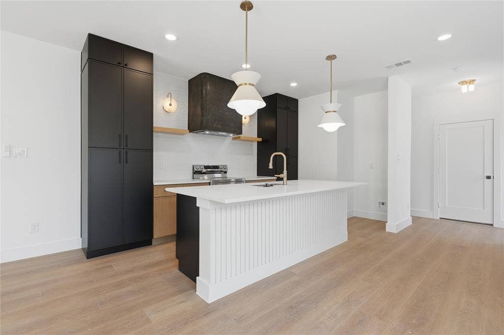 3300 S Harwood Street, Dallas, TX 75215 Modern kitchen featuring a large center island with fluted paneling, light wood-finish flooring, matte black cabinetry, and gold-tone pendant lighting