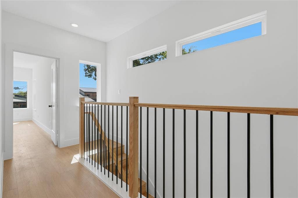 3300 S Harwood Street, Dallas, TX 75215 Light wood-finish flooring, contemporary black metal and wood balustrade, recessed ceiling lighting, multiple windows providing natural illumination, and white interior walls