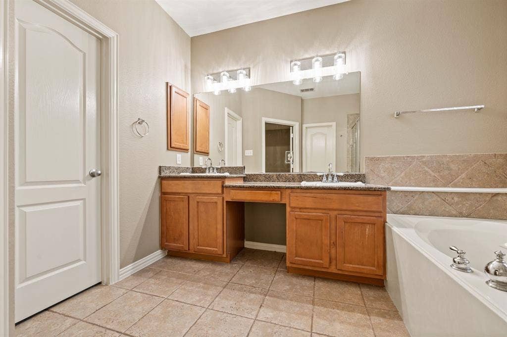 6201 Crator Drive, McKinney, TX 75070 Tile flooring, double vanity with integrated sinks, wood cabinetry, stone countertop, and a built-in bathtub