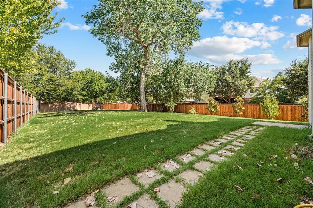 6201 Crator Drive, McKinney, TX 75070 Expansive grassy yard with a new board on board wooden privacy fence, mature trees, and a stone paver pathway