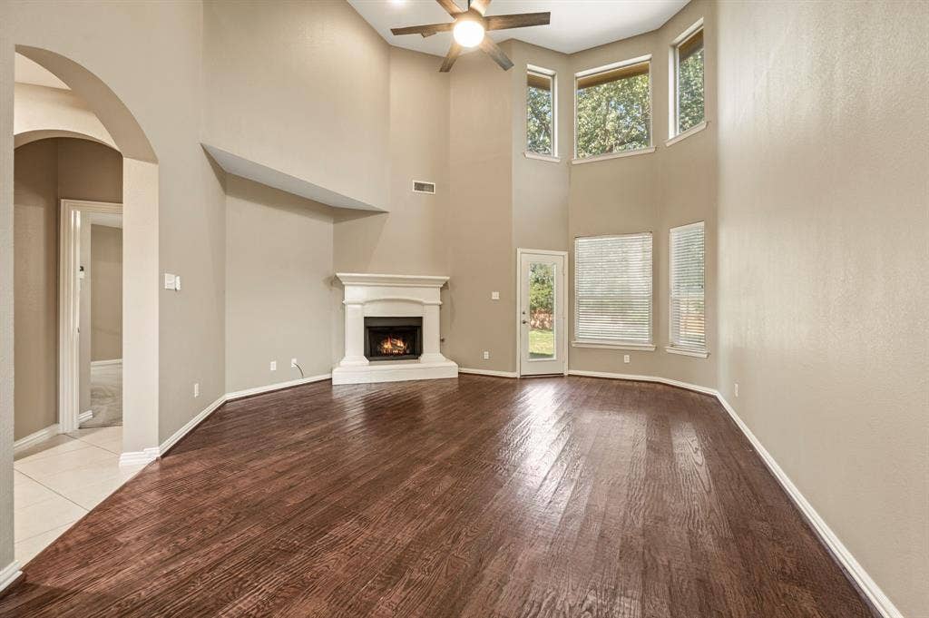 6201 Crator Drive, McKinney, TX 75070 Hardwood flooring throughout, a vaulted ceiling, a fireplace with a white mantel, and multiple windows providing natural light but shaded to keep it cool.