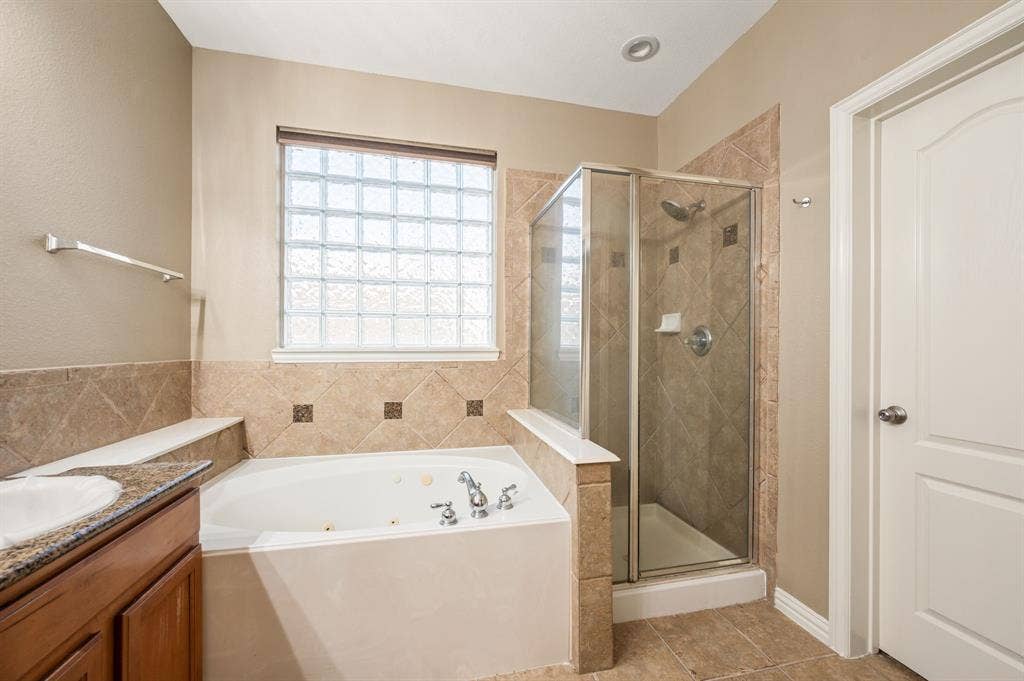 6201 Crator Drive, McKinney, TX 75070 Soaking tub with chrome fixtures, glass block window, tiled shower enclosure, and wood-finish vanity with granite countertops