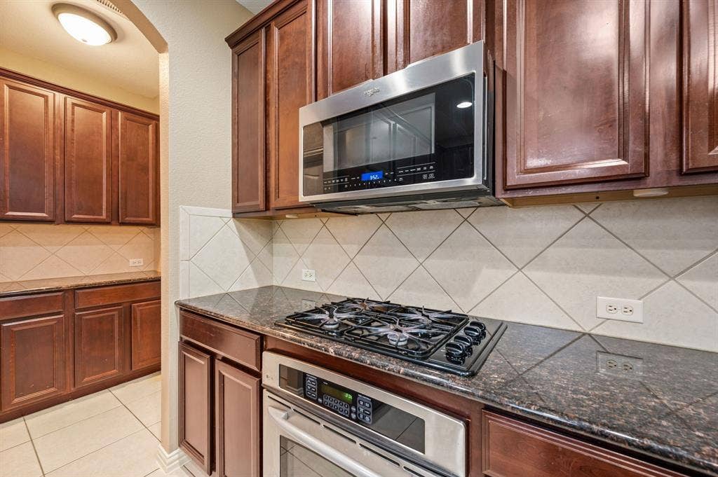 6201 Crator Drive, McKinney, TX 75070 Rich wood cabinetry, granite countertops, tile backsplash, stainless steel built-in microwave, and a gas range
