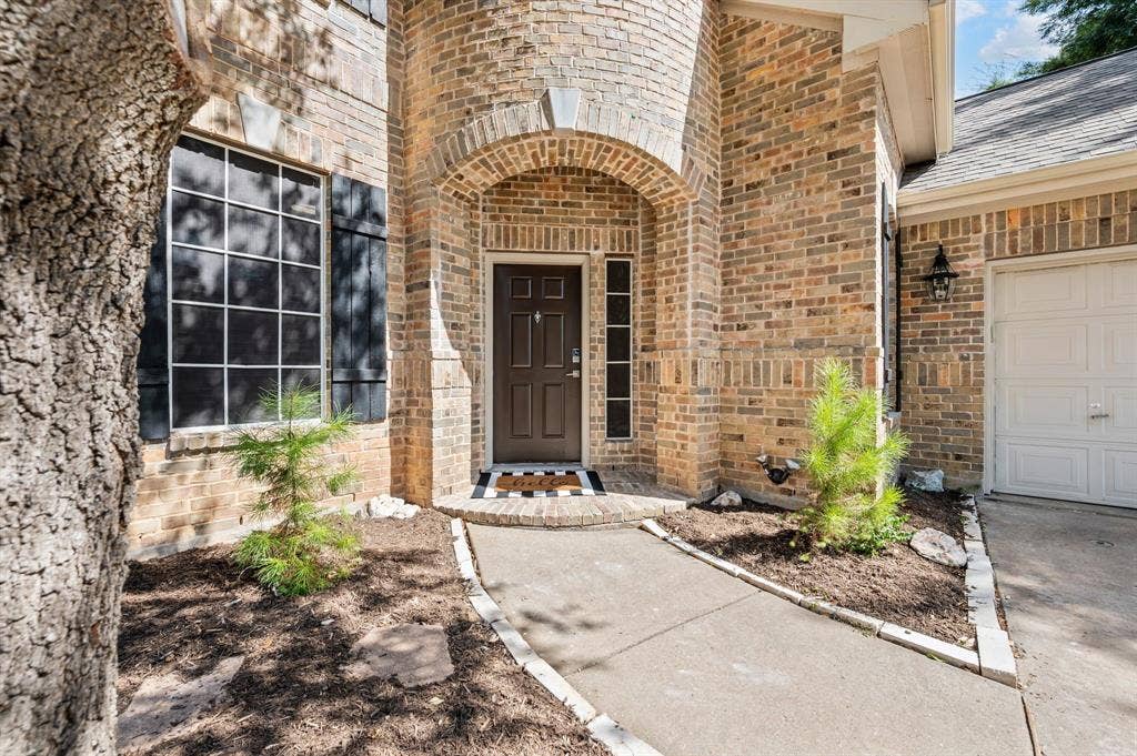 6201 Crator Drive, McKinney, TX 75070 Welcoming brick entry courtyard featuring a rounded archway entrance with freshly patent wood door, mature trees, and low-maintenance landscape beds