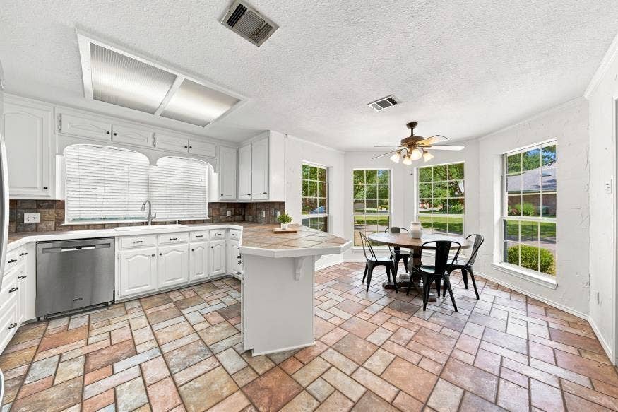 512 Meadowland Drive, Waco, TX 76657 White cabinetry with dark hardware, stainless steel dishwasher, dual basin sink, integrated island with counter seating, and multi-tone tile flooring