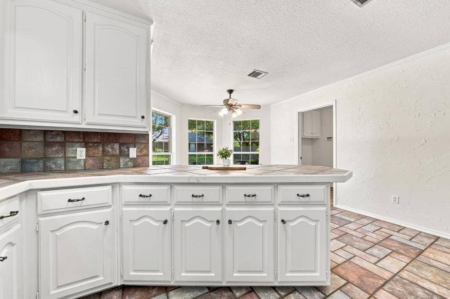 512 Meadowland Drive, Waco, TX 76657 White cabinetry with dark hardware, multicolored tile backsplash, and a breakfast bar
