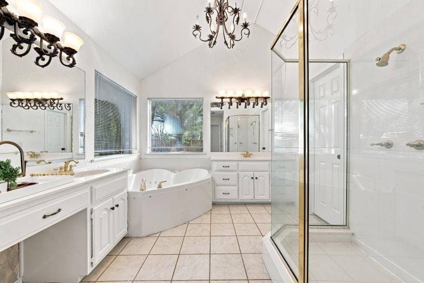 512 Meadowland Drive, Waco, TX 76657 Dual vanity with gold-finish fixtures and white cabinetry, separate glass-enclosed shower, jetted soaking tub, tiled flooring, and vaulted ceiling