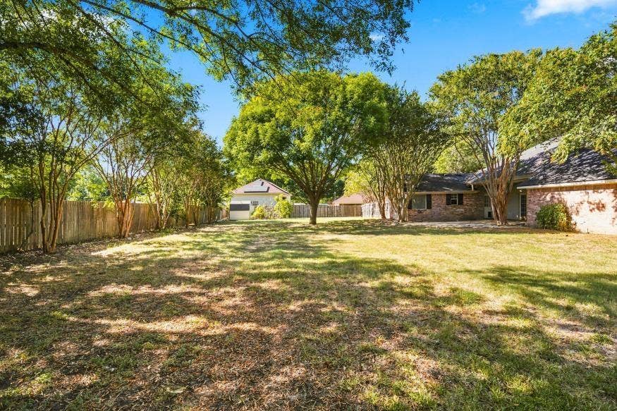 512 Meadowland Drive, Waco, TX 76657 Expansive backyard with a manicured lawn, mature trees, and a wooden privacy fence