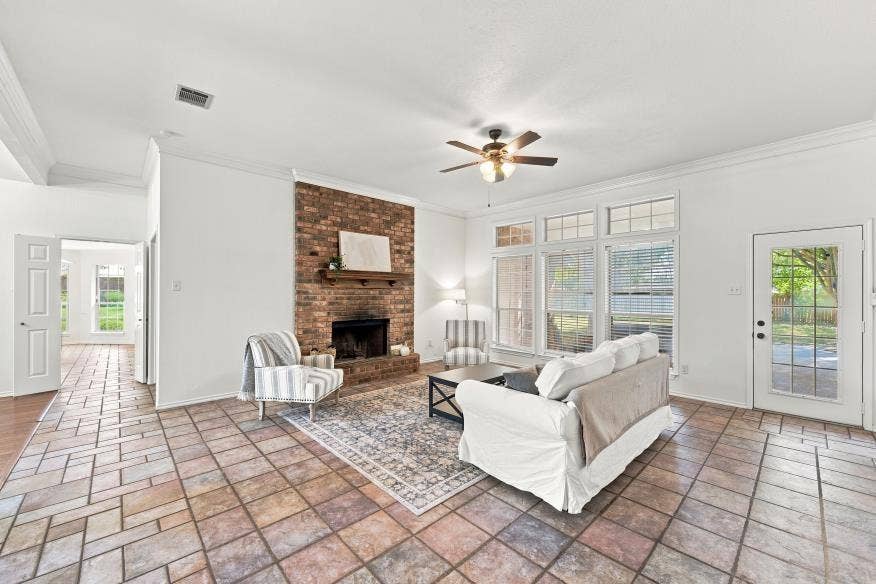 512 Meadowland Drive, Waco, TX 76657 Exposed brick fireplace with a wood mantle, ceiling fan, tile flooring, glass-paned exterior door, and multiple windows