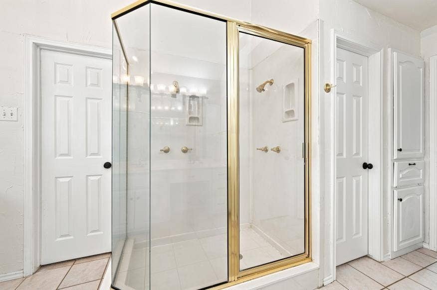 512 Meadowland Drive, Waco, TX 76657 Glass-enclosed shower with gold-tone framing and hardware, integrated shower niche, and tile flooring