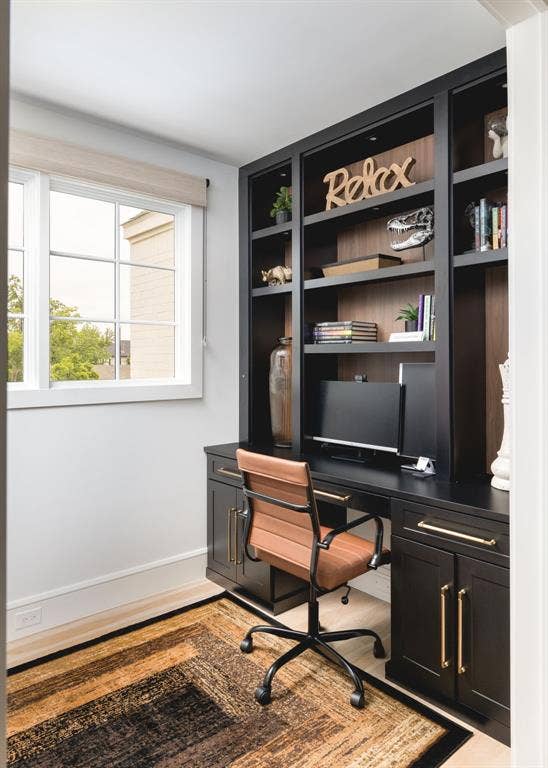 Built-in black cabinetry with gold-finish hardware, integrated desk space, upper shelving with recessed lighting, and wood-finish flooring