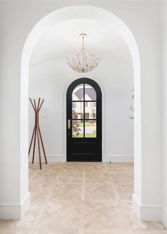 Arched entryway featuring a black arched door with glass panes, a decorative chandelier, and light wood-finish flooring with a geometric pattern