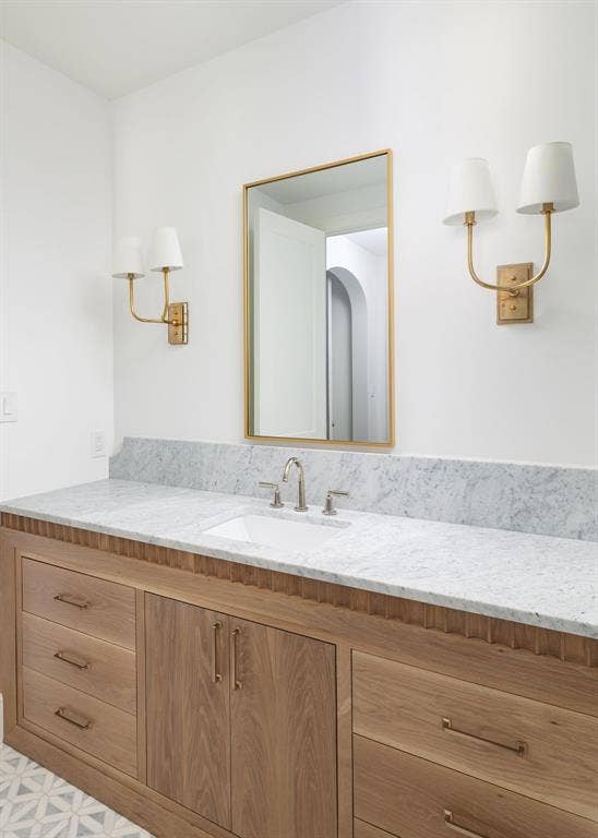 Custom wood vanity with brass hardware, undermount sink, stone countertop, and decorative wall sconces