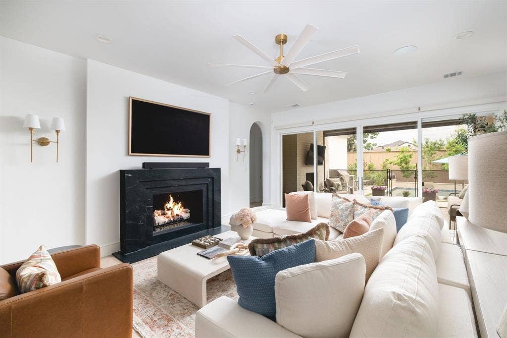 Recessed lighting, ceiling fan, fireplace with dark stone surround, wall sconces, and sliding glass doors to the exterior
