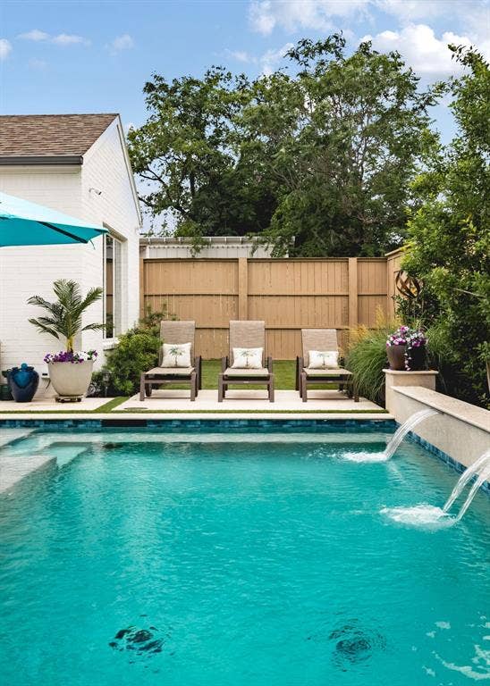 Pool with integrated water features and steps, surrounded by a wood privacy fence and artificial turf