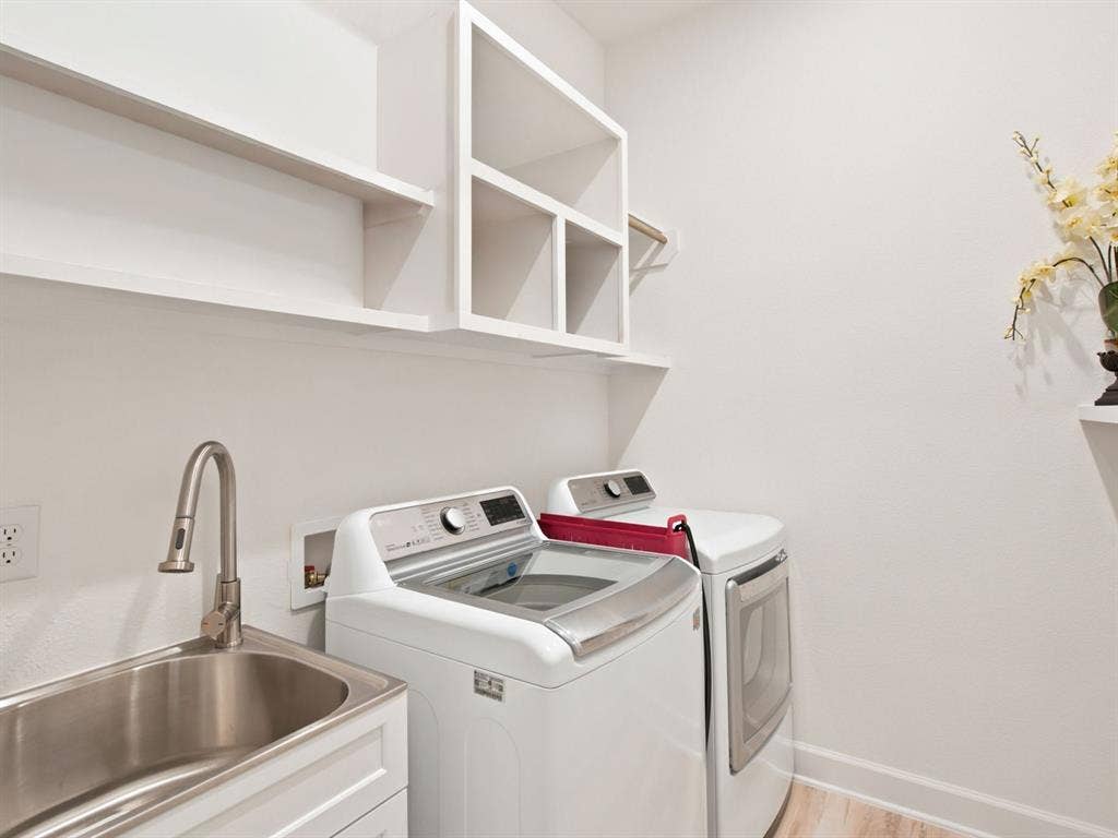 Laundry room with a stainless steel utility sink, a gooseneck faucet, white shaker cabinetry, and open shelving