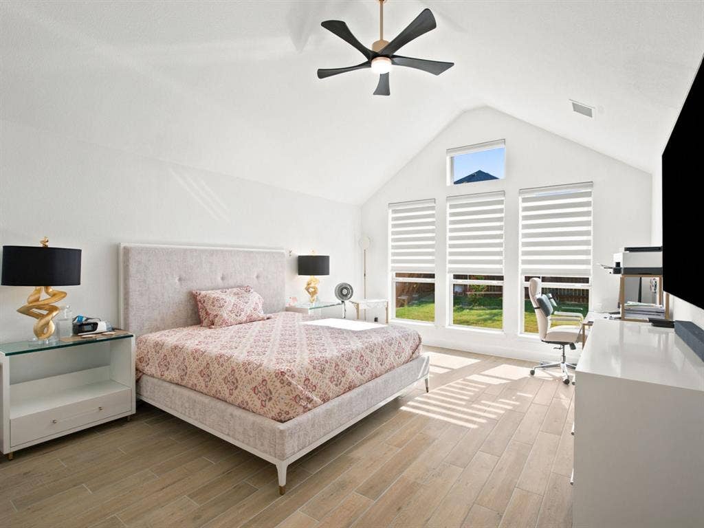 Vaulted ceiling, modern ceiling fan, three large windows with blinds, wood-finish flooring, and additional window above