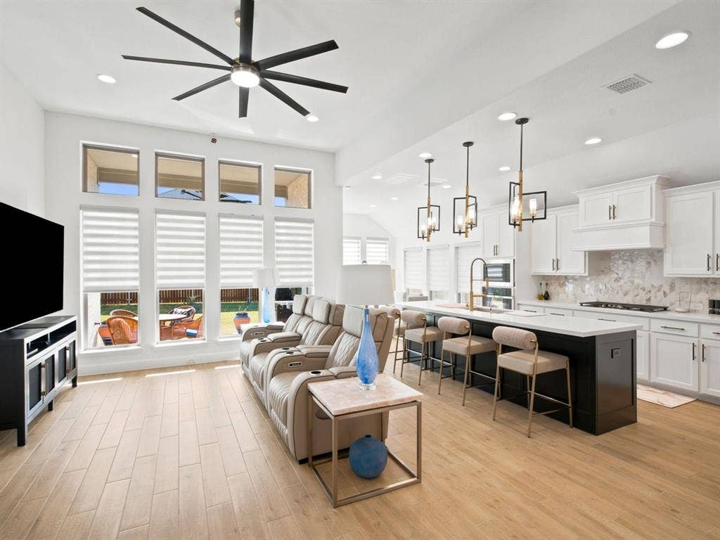 Open-concept living space with wood-finish flooring, a contemporary ceiling fan, and large windows