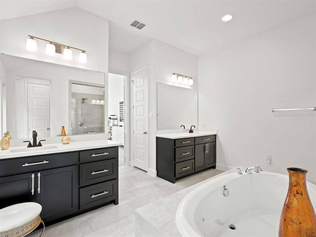 Dual vanities with dark cabinetry and white countertops, large soaking tub, and tiled flooring